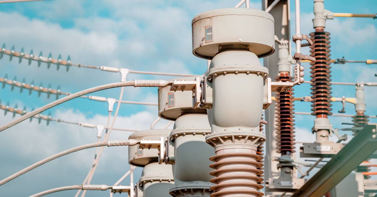 Several transformers in a row connected to power lines outdoors at an electrical substation with a blue cloudy sky.