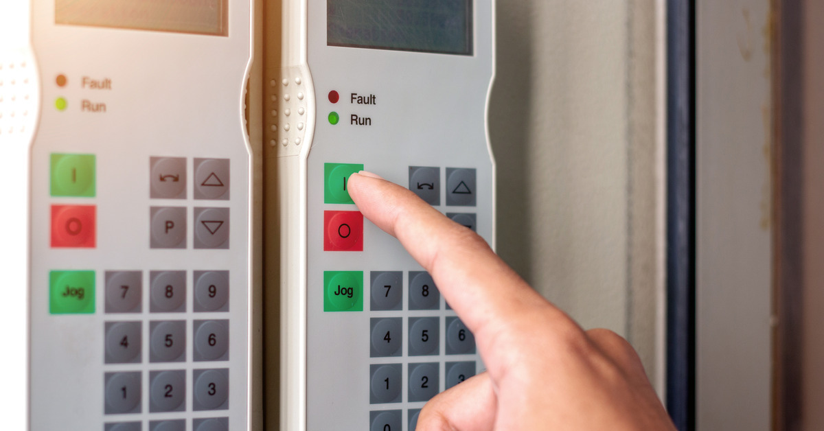 A person's finger presses a green button on a rectangular panel with an LCD screen on a frequency converter.