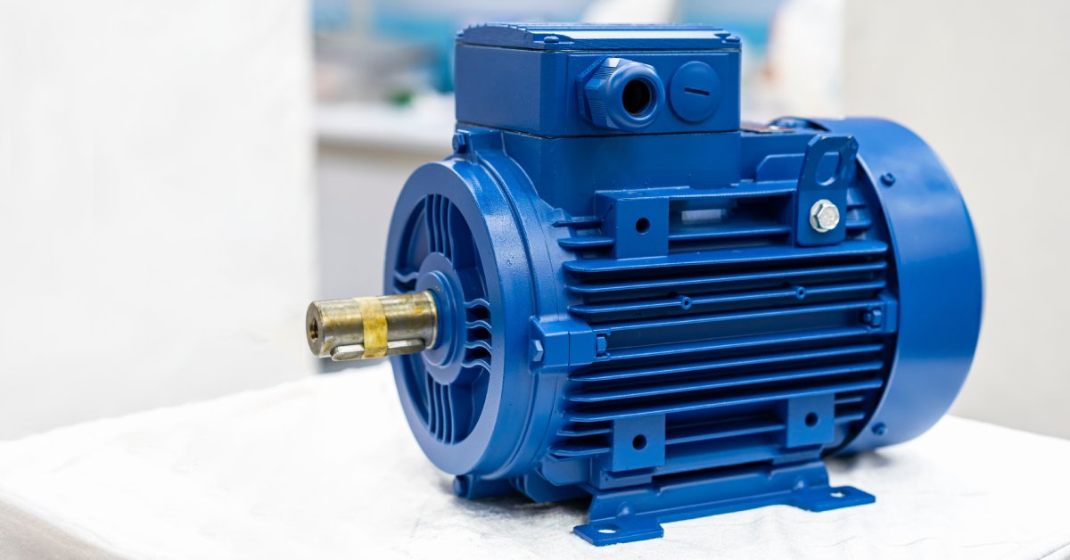A blue electric induction motor for industrial use sits on a white pedestal with a blurred background.
