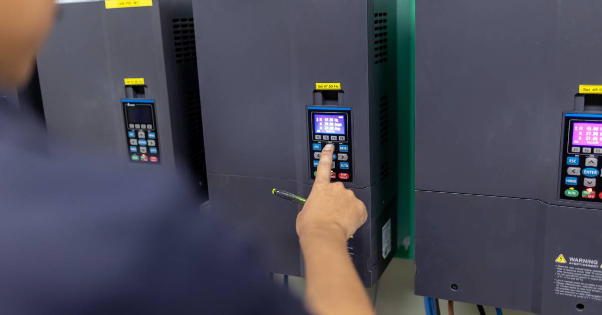 A worker presses a button on a frequency converter control panel to adjust a parameter on the lit display.