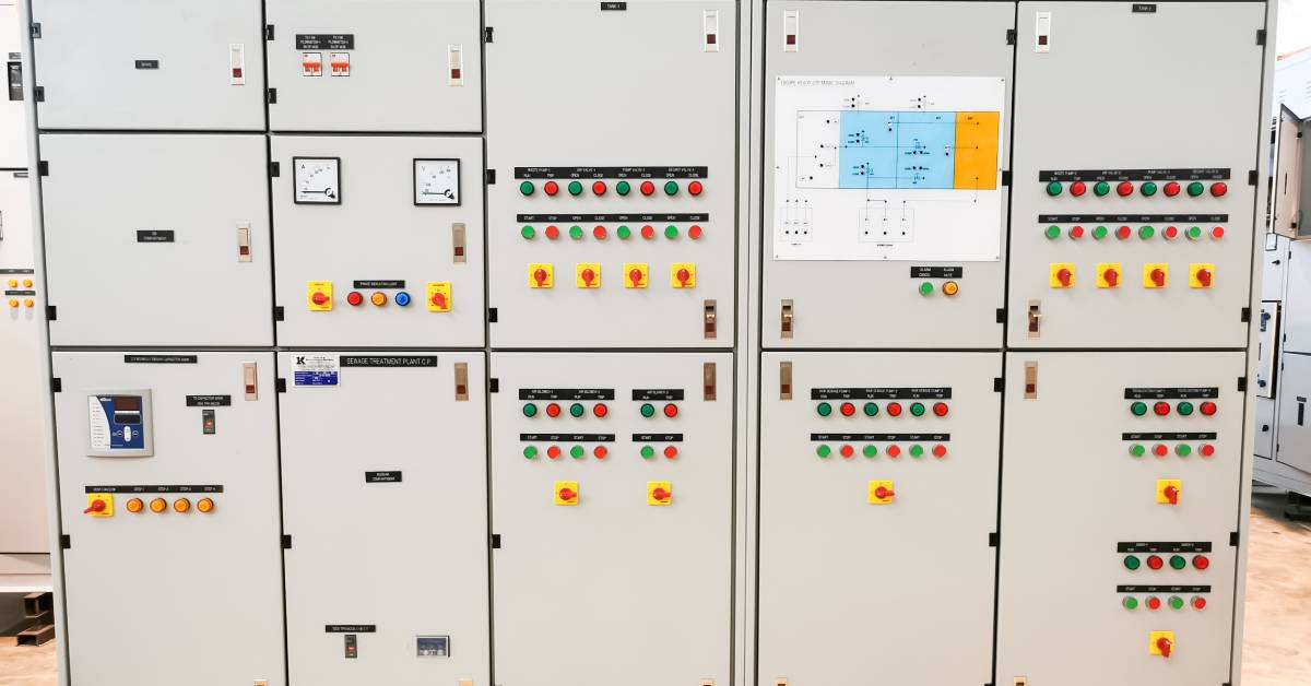A large gray control panel cabinet with multicolored circular buttons and switches in a sewage treatment plant.